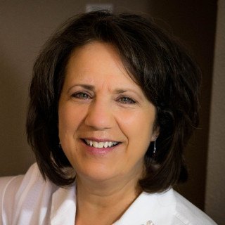 Head shot of a light skin toned woman with black hair wearing a white blouse.